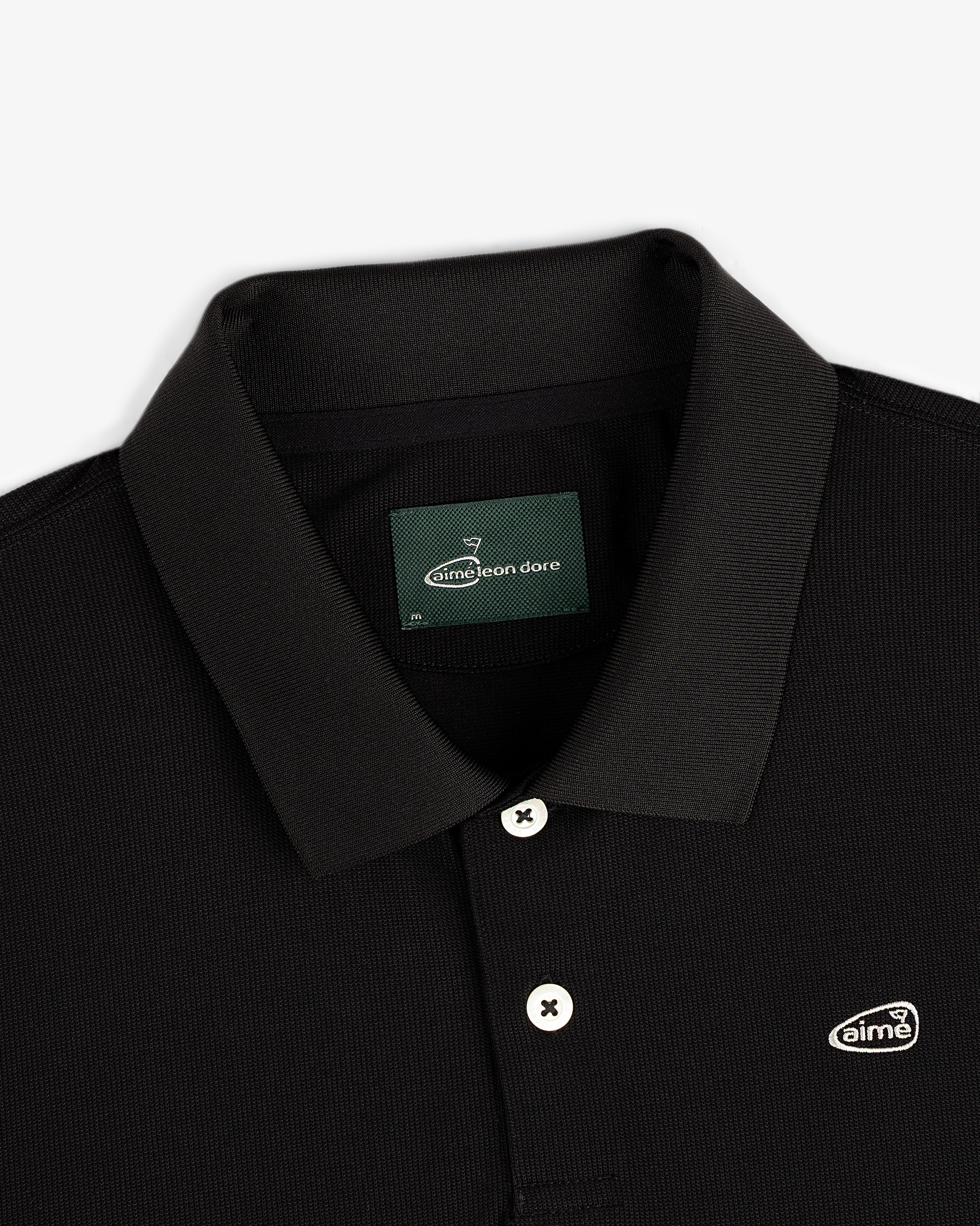 ALD Golf Polo: black collared shirt with white buttons and Aimé Leon Dore logo patch on the chest.