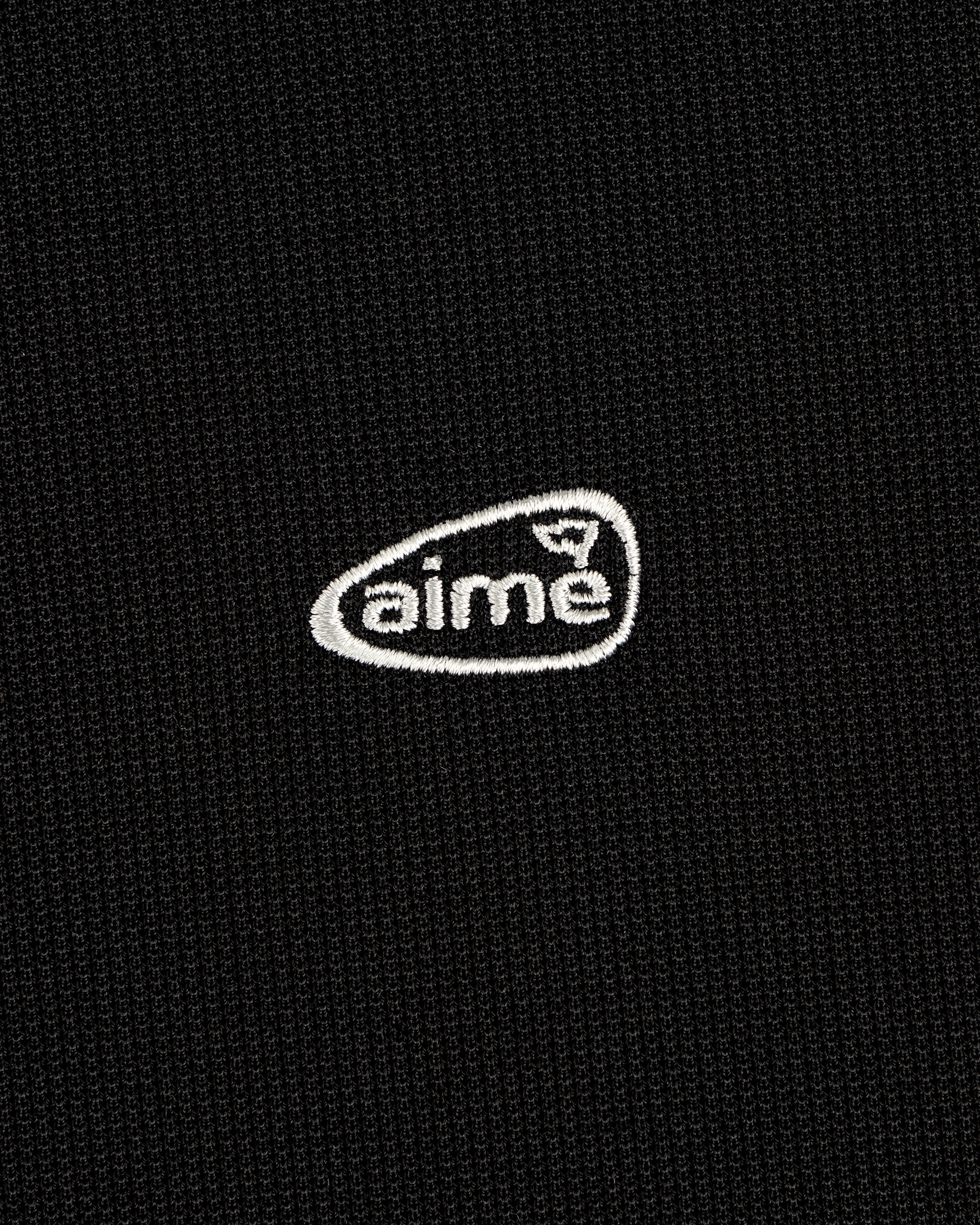 A small white aime logo is embroidered on a textured black ALD Golf Polo.