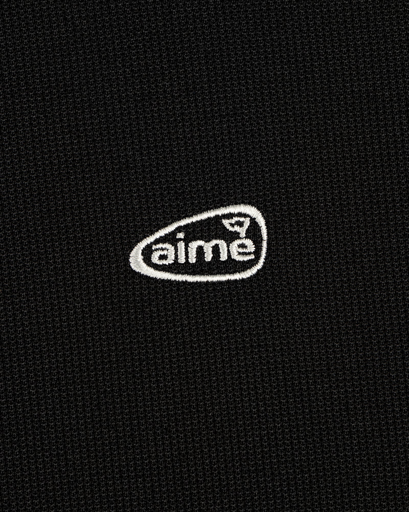 A small white aime logo is embroidered on a textured black ALD Golf Polo.