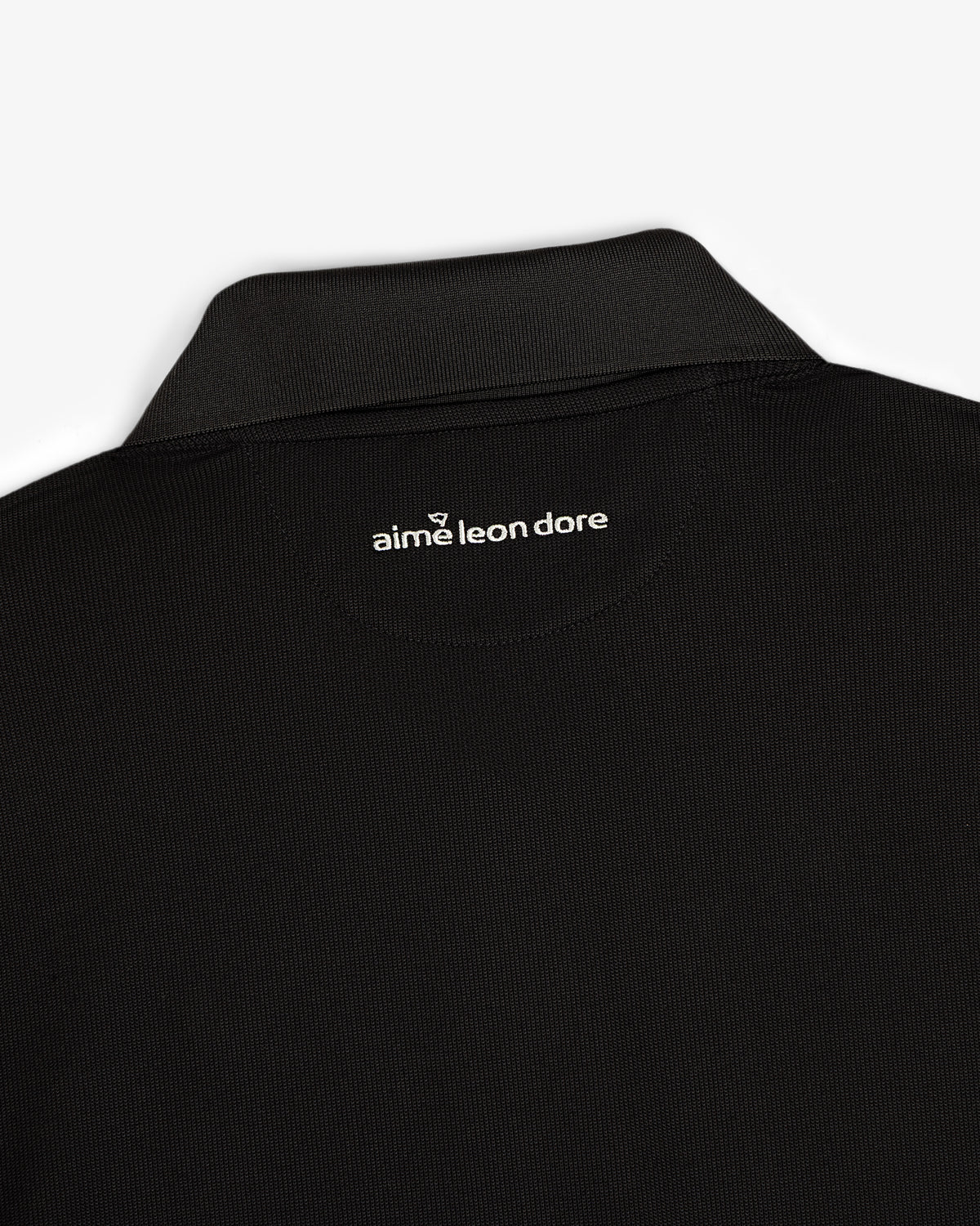 Close-up of the back collar of the ALD Golf Polo with "aime leon dore" printed in white below the neckline.