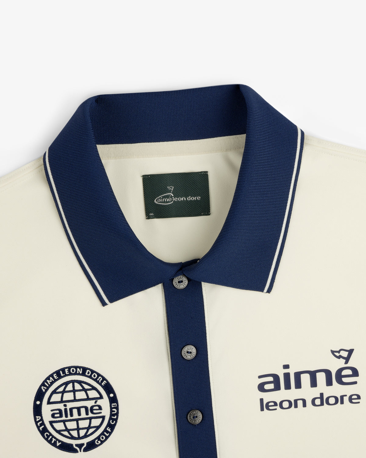 Cream ALD Golf Tour Polo with navy collar, Aimé Leon Dore logo and globe chest graphic, shown flat.