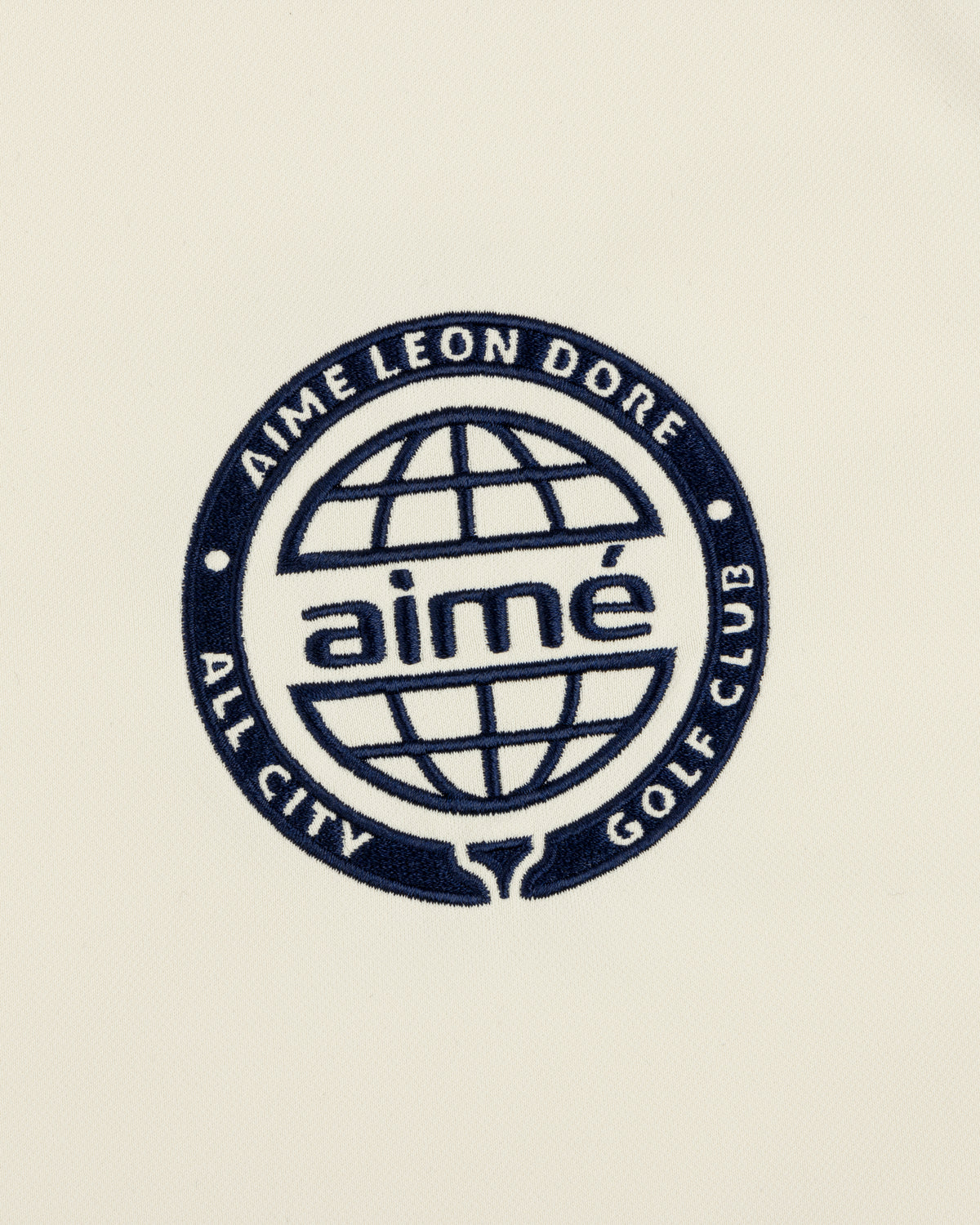 Navy blue globe logo with “AIMÉ LEON DORE ALL CITY GOLF CLUB” and “aimé” on cream ALD Golf Tour Polo.