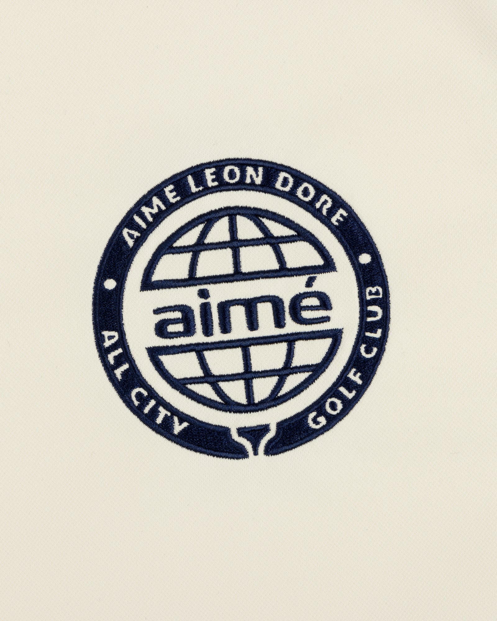 Navy blue globe logo with “AIMÉ LEON DORE ALL CITY GOLF CLUB” and “aimé” on cream ALD Golf Tour Polo.