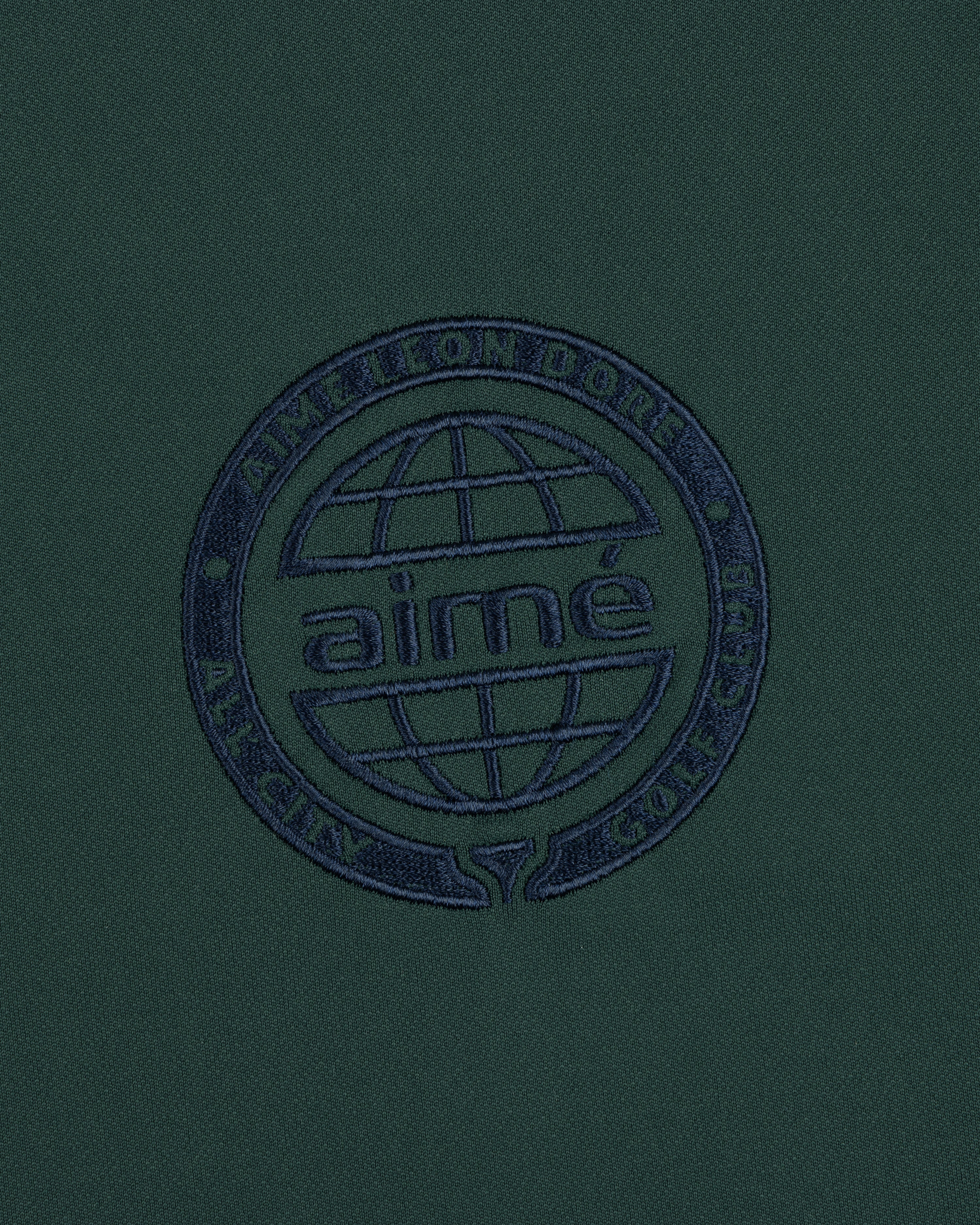 The ALD Golf Tour Polo features dark green fabric with a navy globe logo and Aimé Leon Dore All City Golf Club text.