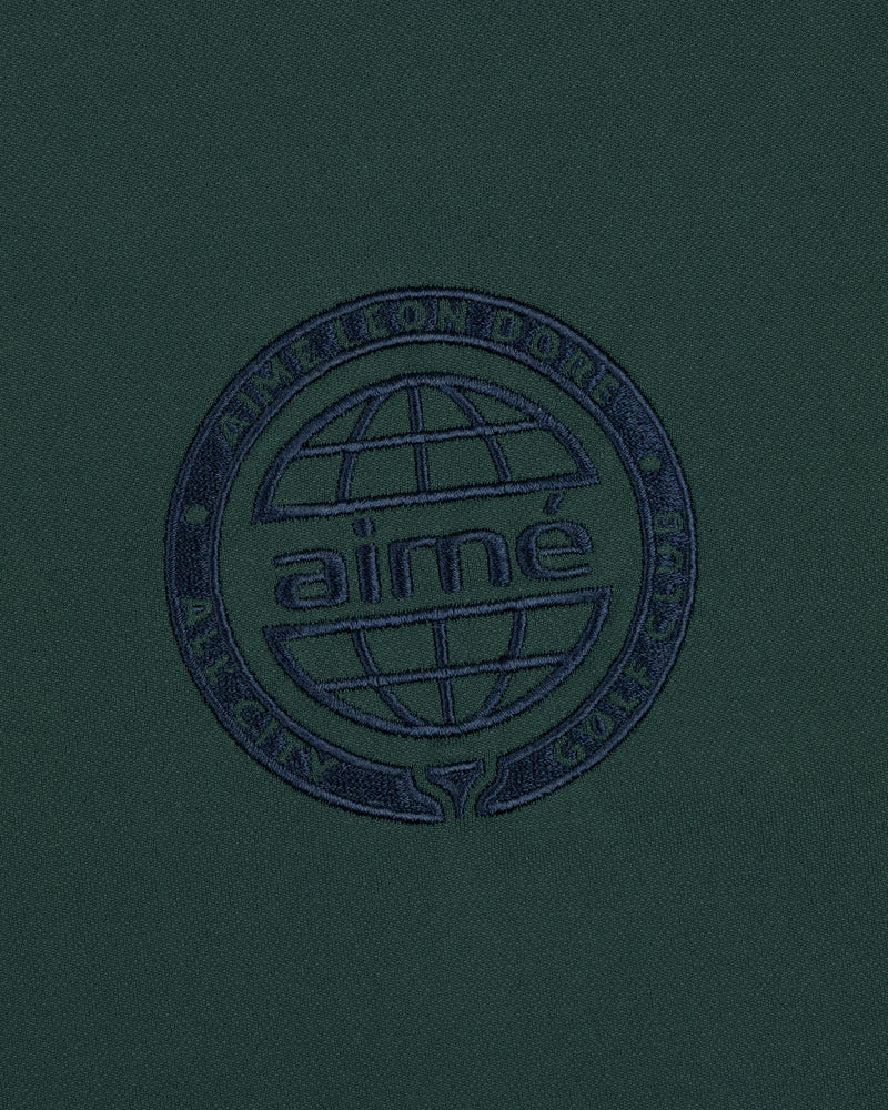 The ALD Golf Tour Polo features dark green fabric with a navy globe logo and Aimé Leon Dore All City Golf Club text.