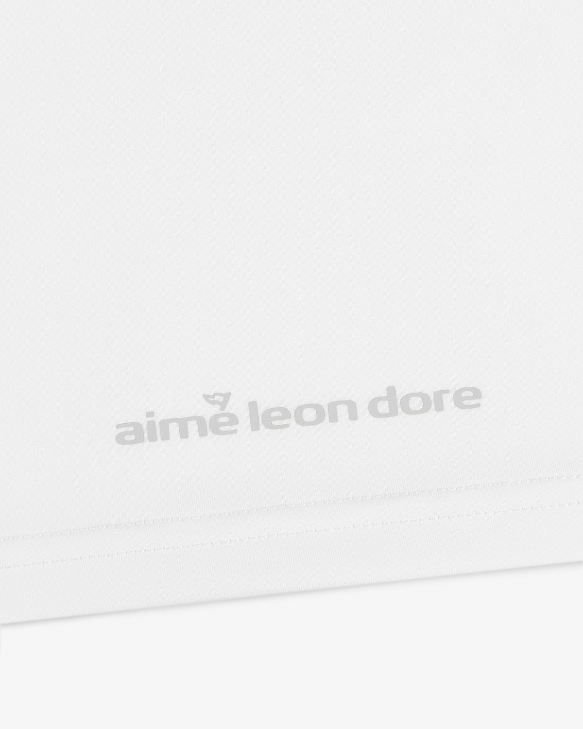 Close-up of the ALD Golf Performance Tee's white fabric featuring gray "aime leon dore" text near the bottom edge.