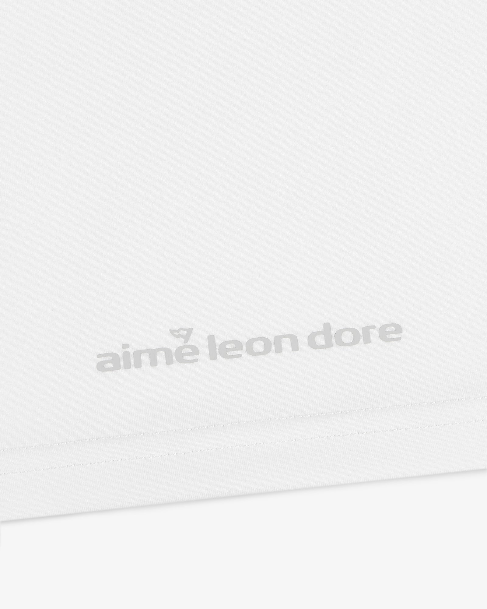 Close-up of the ALD Golf Performance Tee's white fabric featuring gray "aime leon dore" text near the bottom edge.