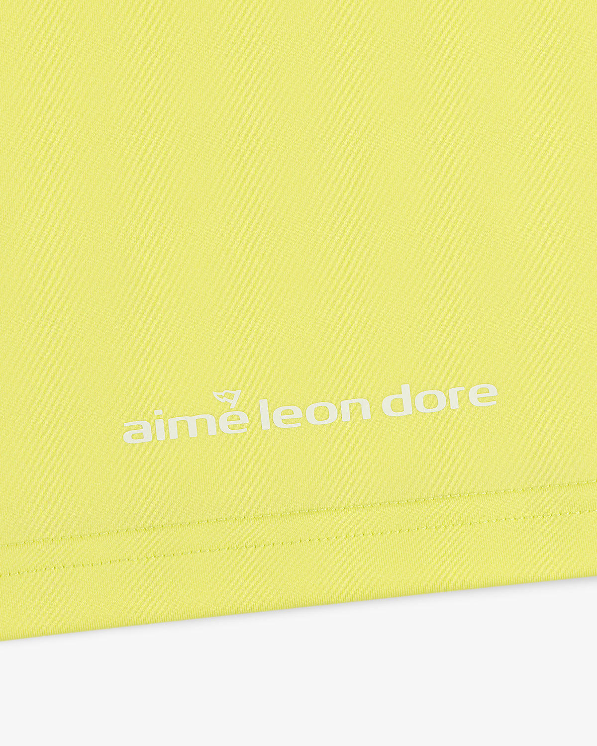 Close-up of a yellow ALD Golf Performance Tee with "aime leon dore" printed in white near the bottom edge.