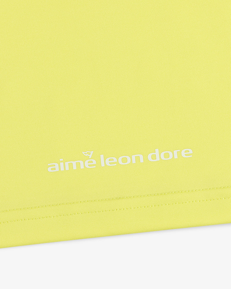 Close-up of a yellow ALD Golf Performance Tee with "aime leon dore" printed in white near the bottom edge.