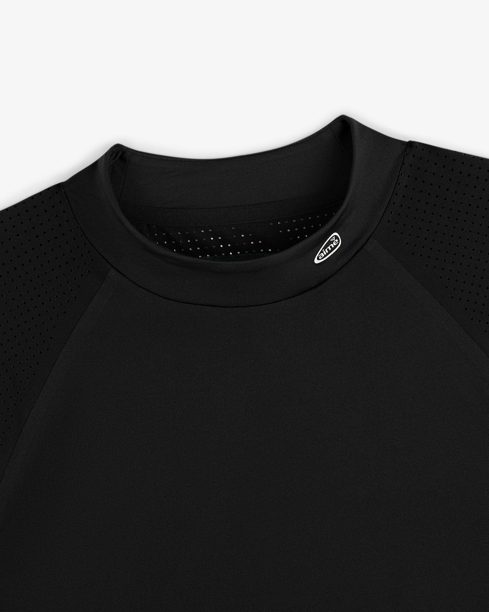 Close-up of the ALD Golf Performance Tee, a black shirt with perforated shoulders and a small oval logo by the collar.