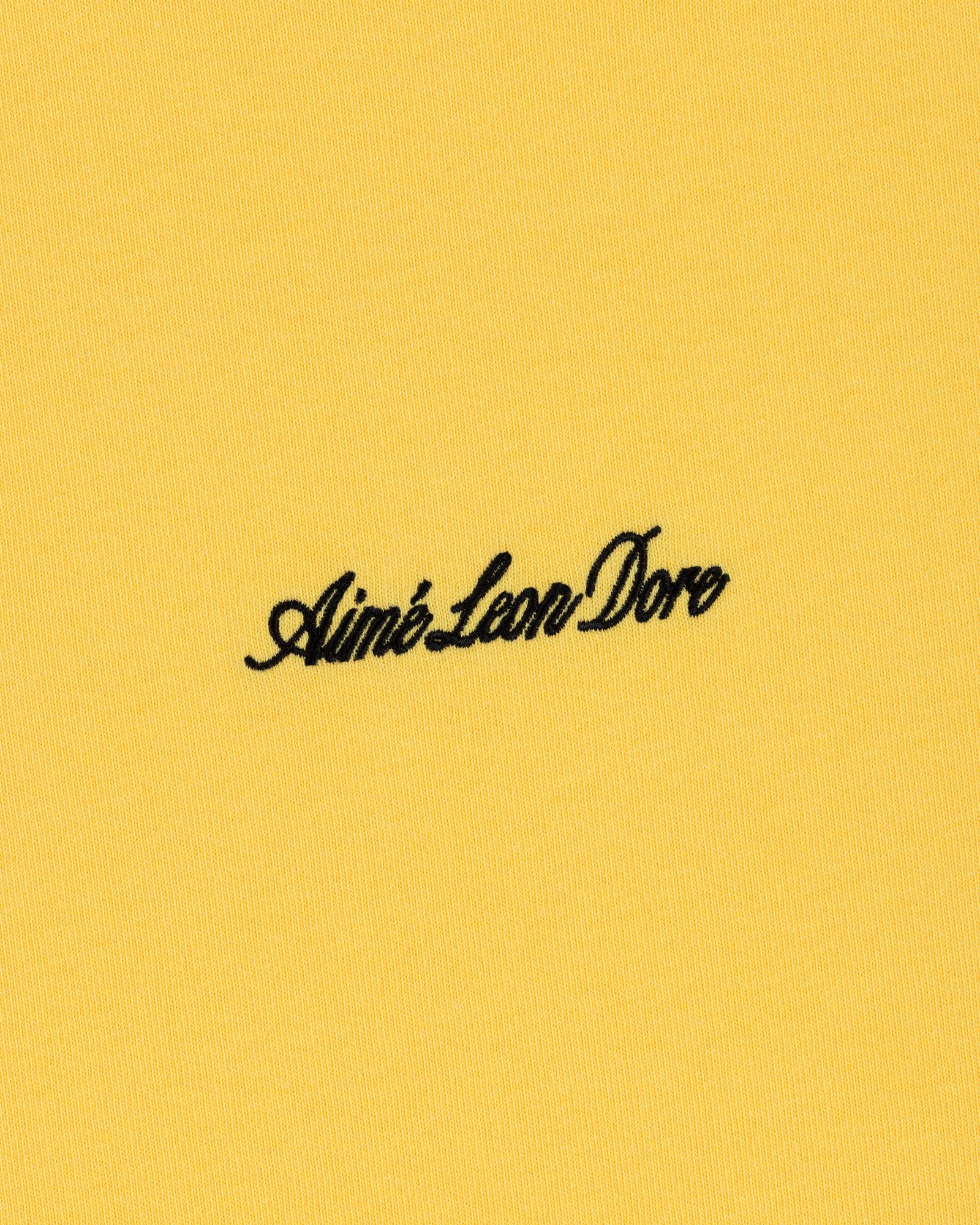 Yellow Embroidered Logo Tee with Aimé Leon Dore in black cursive at the center.