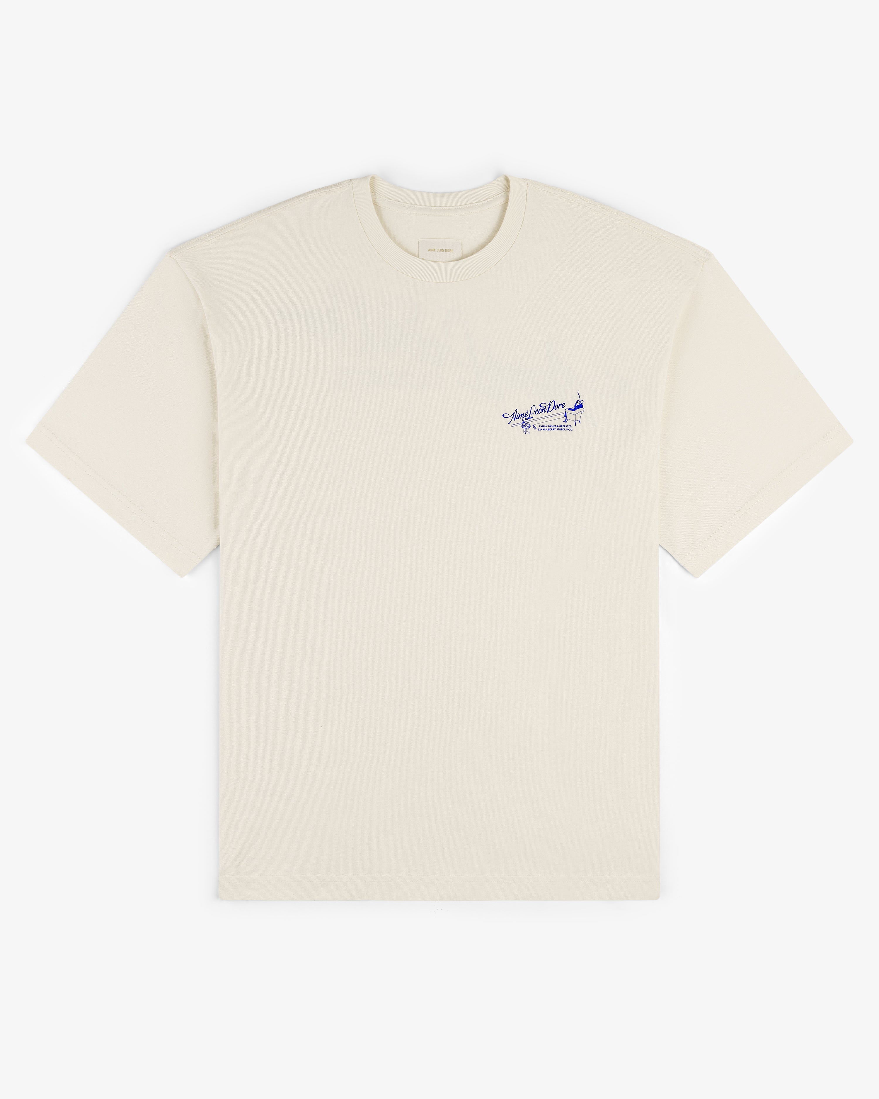 Pappoús Logo Tee—beige short-sleeve shirt with small blue script and graphic on left chest, shown on white.