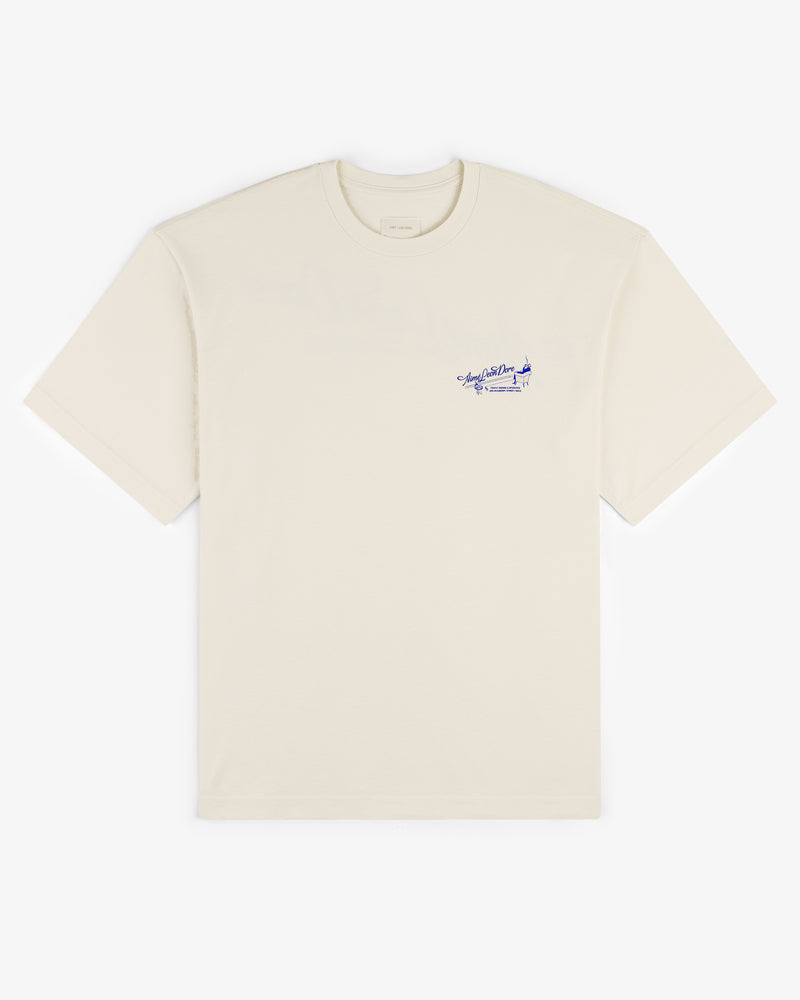 Pappoús Logo Tee—beige short-sleeve shirt with small blue script and graphic on left chest, shown on white.