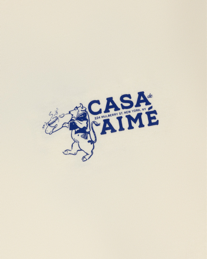 A cartoon dog in a scarf holds bread by "Casa de AIME, 224 Mulberry St. NY" on the Long-Sleeve Casa Tee in blue font.