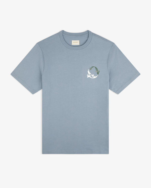 Woodblock Dove Tee: light blue short-sleeve shirt with a white bird and green leaf graphic on the left chest.