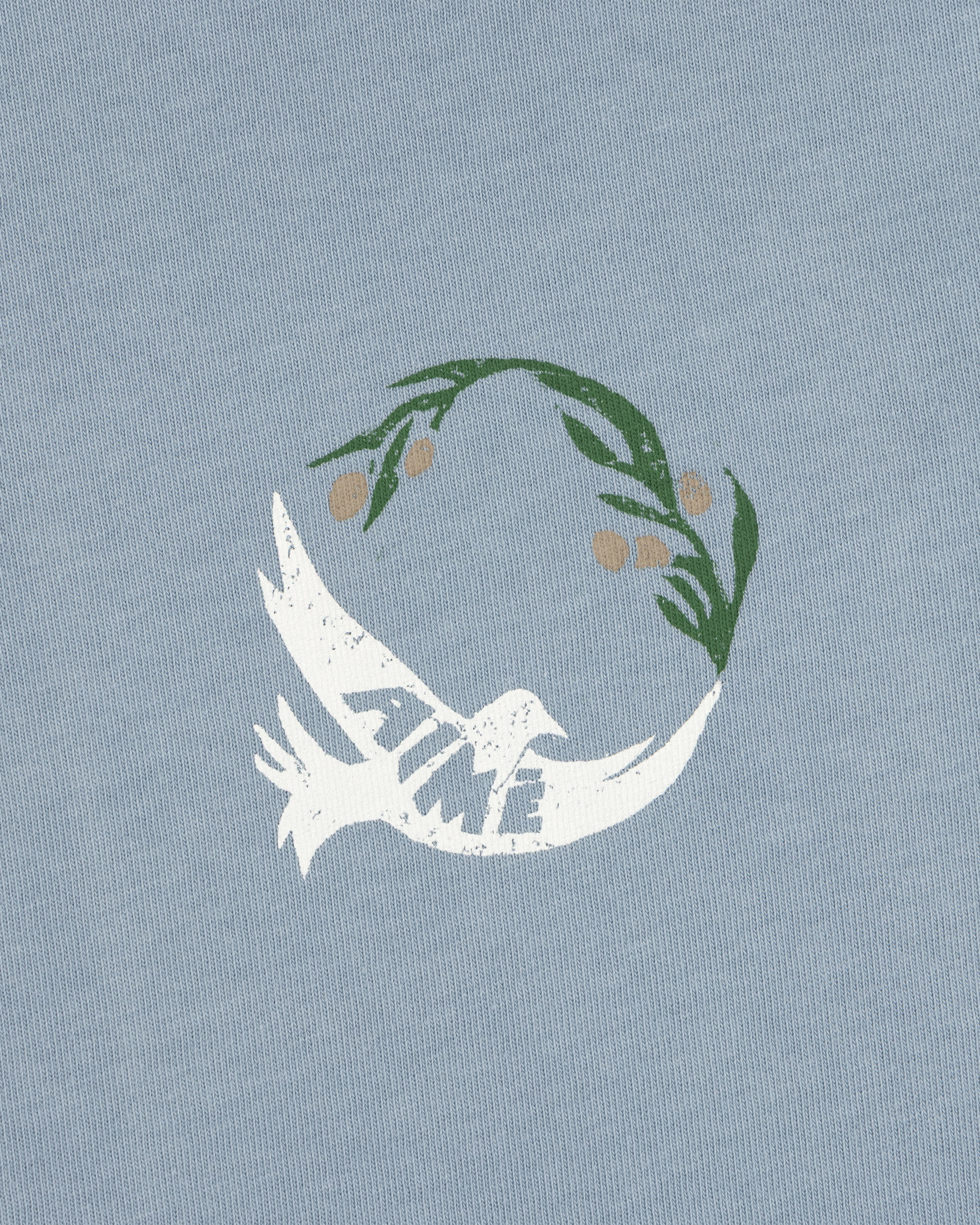 Woodblock Dove Tee features a white dove with TIME on its wing, flying beneath a green olive branch on light blue.