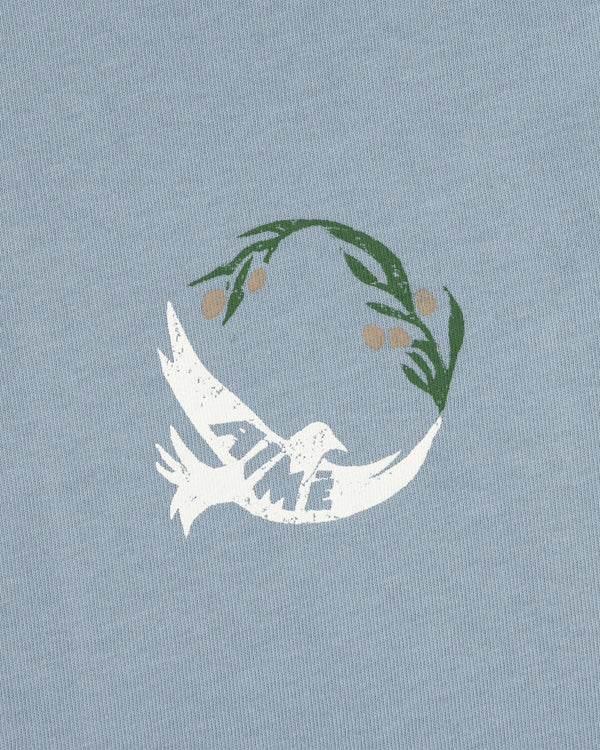 Woodblock Dove Tee features a white dove with TIME on its wing, flying beneath a green olive branch on light blue.