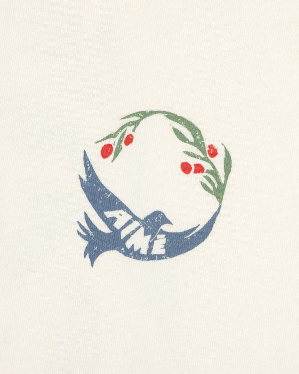 The Woodblock Dove Tee features a blue bird with AIMÉ, holding an olive branch with red berries on a cream background.