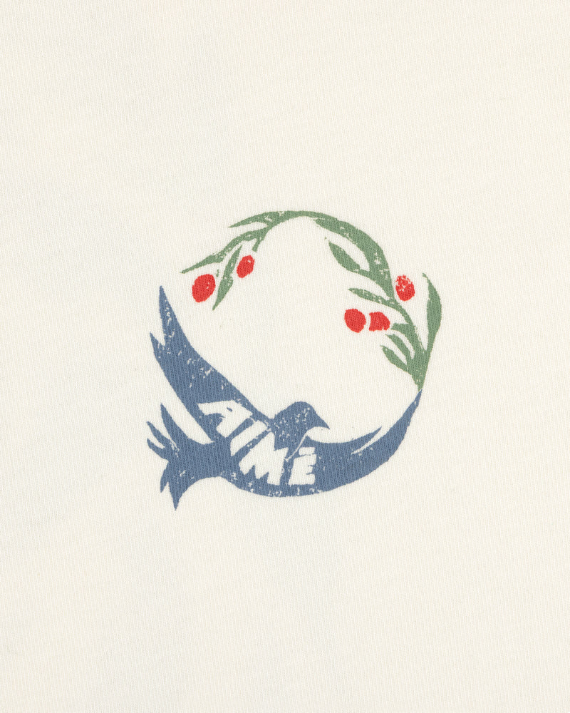 The Woodblock Dove Tee features a blue bird with AIMÉ, holding an olive branch with red berries on a cream background.