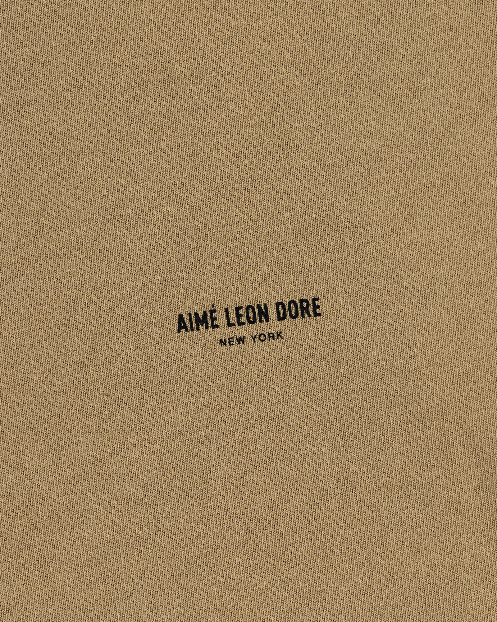 Tan Safari Tee featuring small black text "AIMÉ LEON DORE NEW YORK" printed in the center.