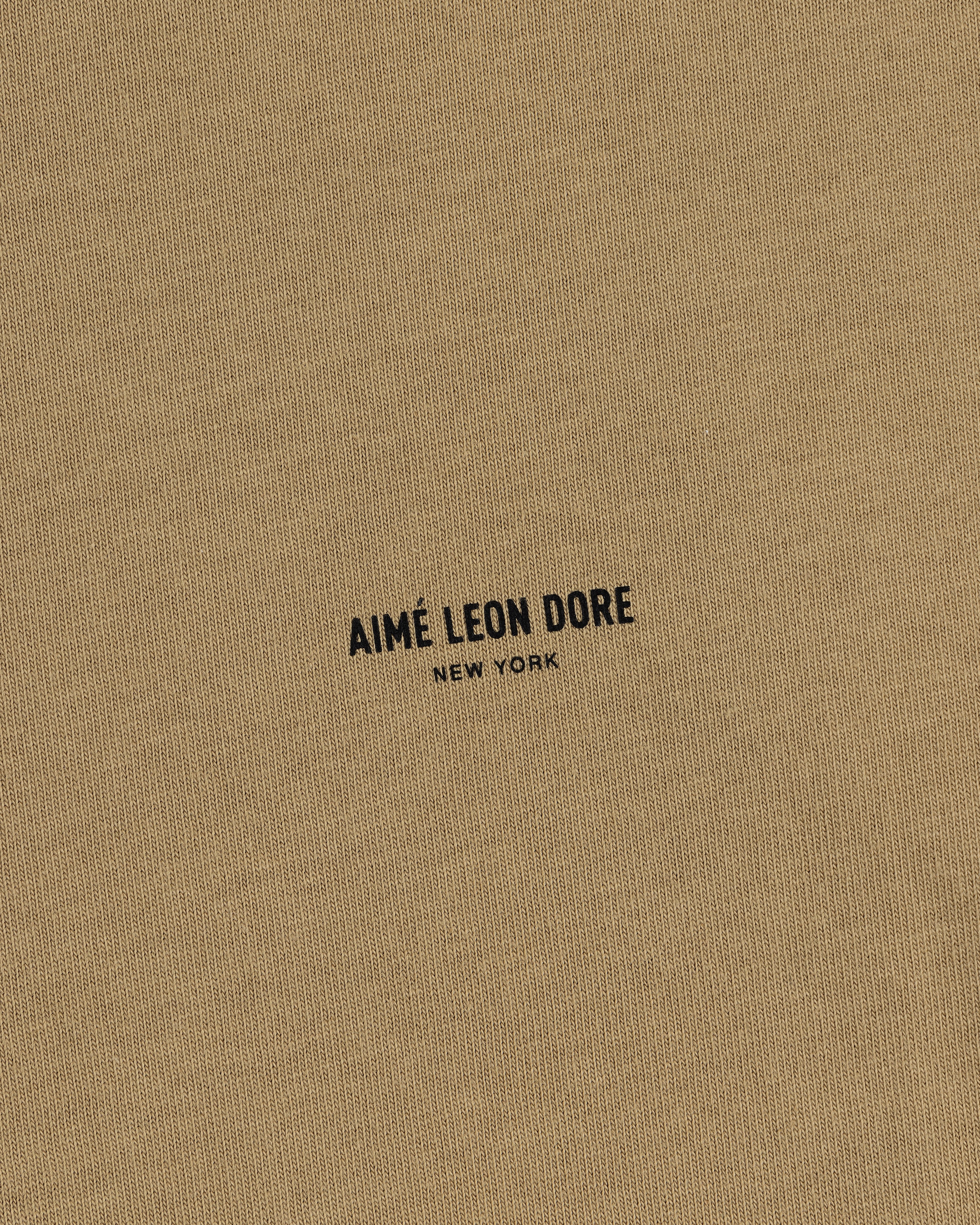 Tan Safari Tee featuring small black text "AIMÉ LEON DORE NEW YORK" printed in the center.