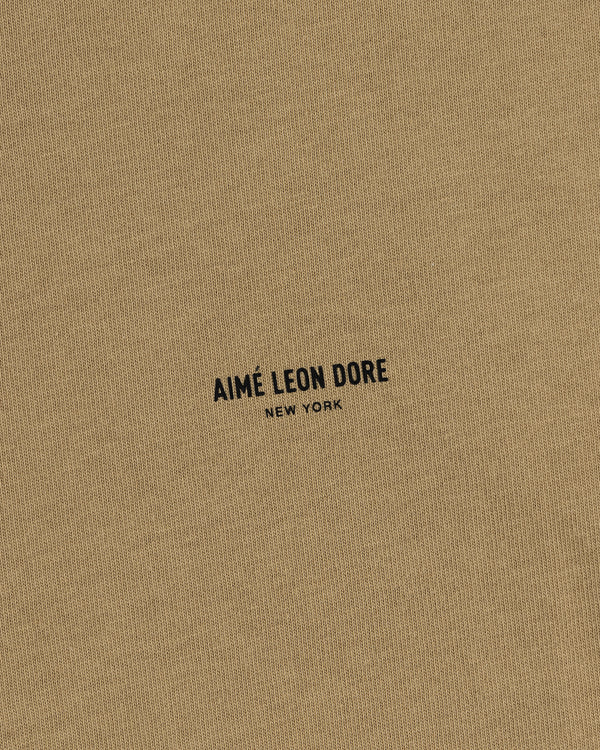 Tan Safari Tee featuring small black text "AIMÉ LEON DORE NEW YORK" printed in the center.