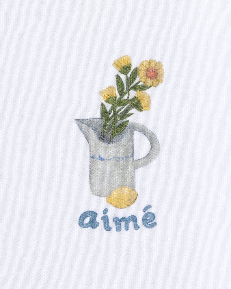 Breakfast Tee featuring a yellow flower pitcher and lemon with "aimé" below on a white background.