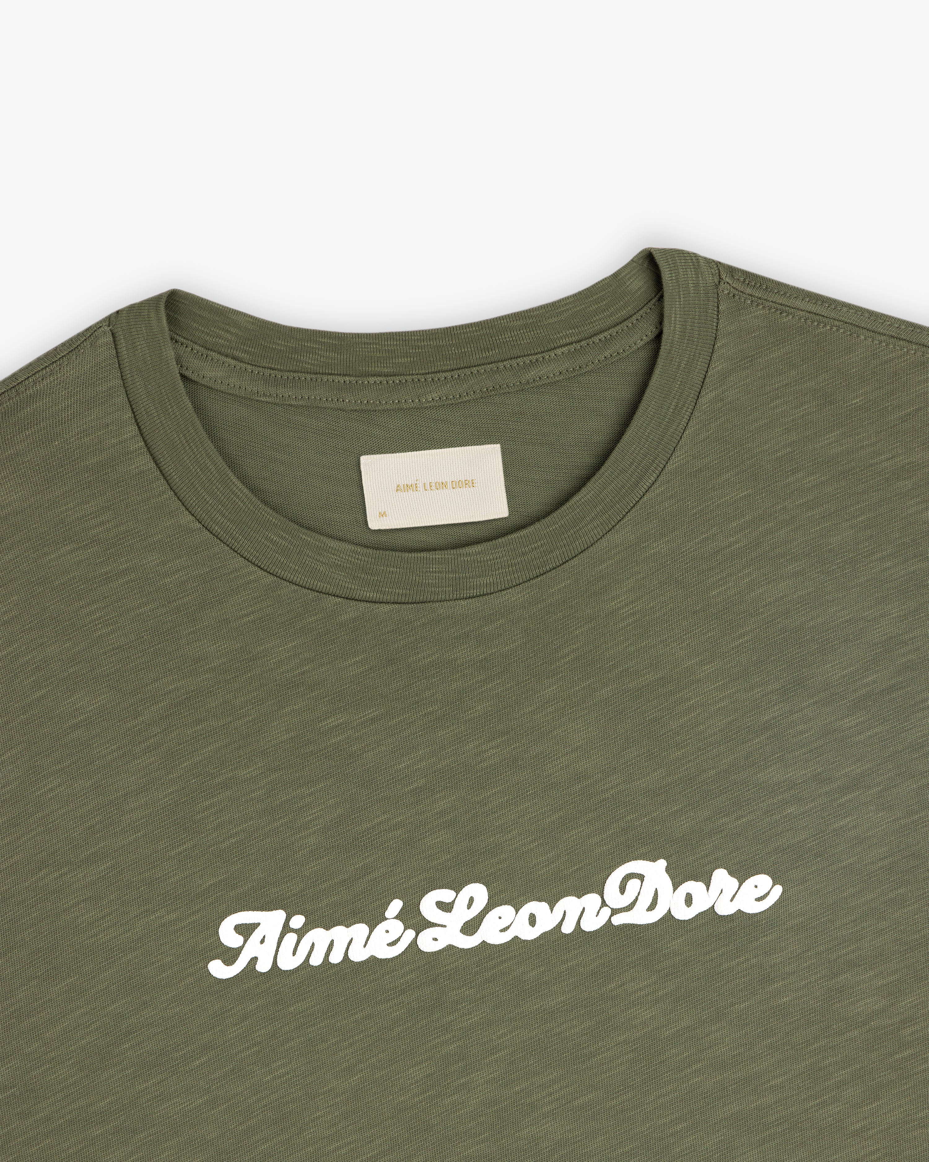 Olive green Puff Print Slub Logo Tee with Aimé Leon Dore in white script across the chest.