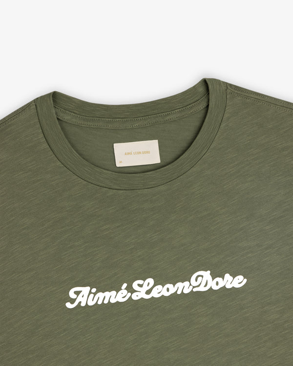 Olive green Puff Print Slub Logo Tee with Aimé Leon Dore in white script across the chest.