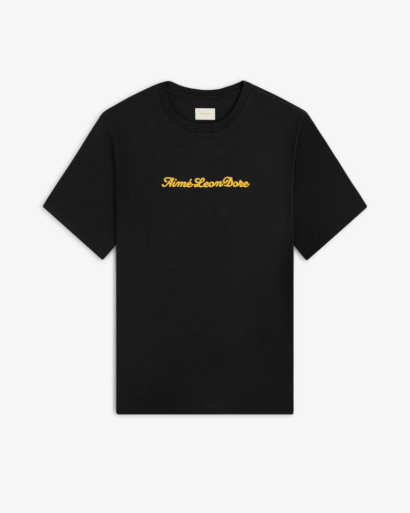 Black Puff Print Slub Logo Tee with yellow Aimé Leon Dore cursive text centered on the chest.