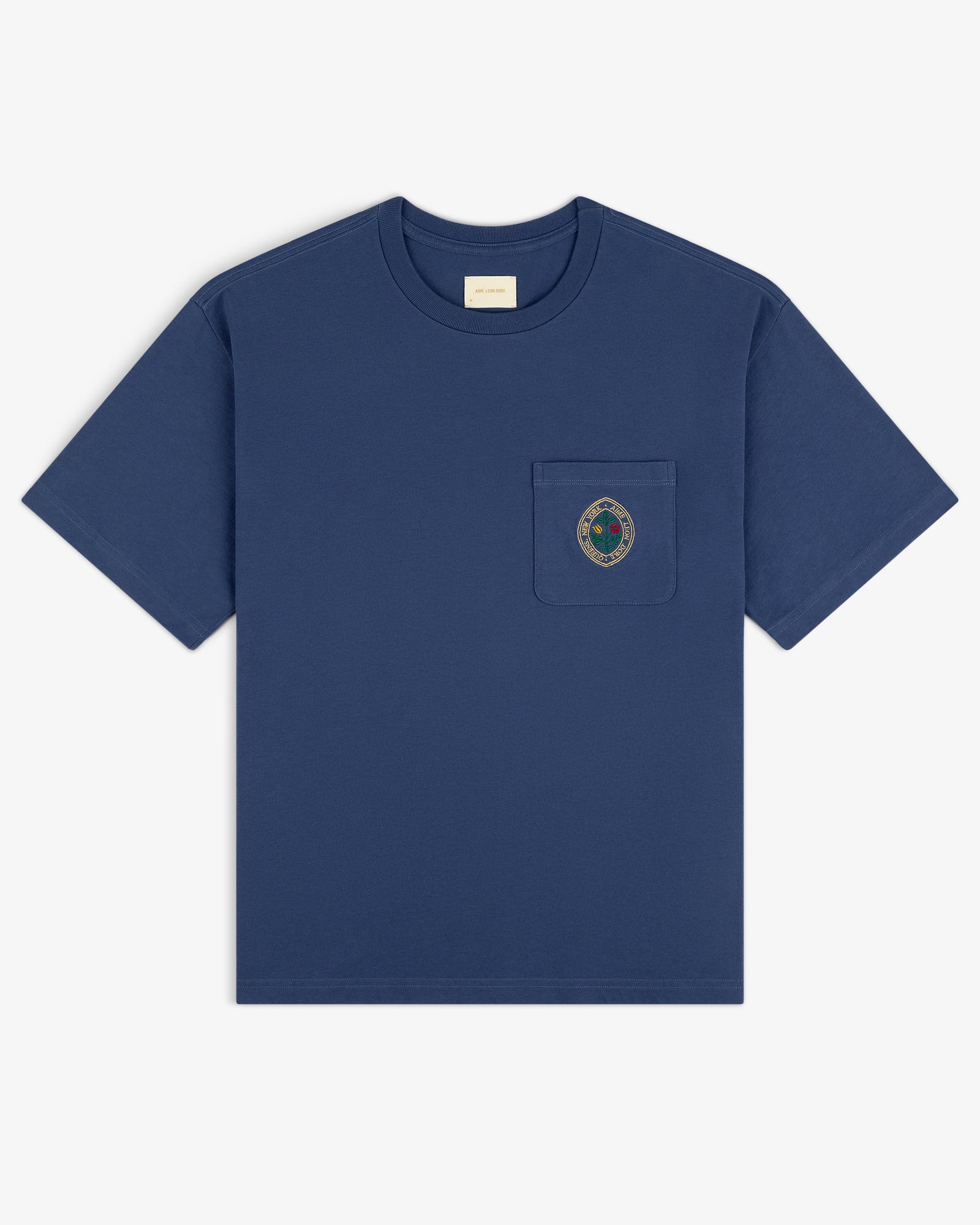 Botanical Crest Pocket Tee: blue short-sleeve shirt with small crest emblem on left chest pocket, shown on white background.