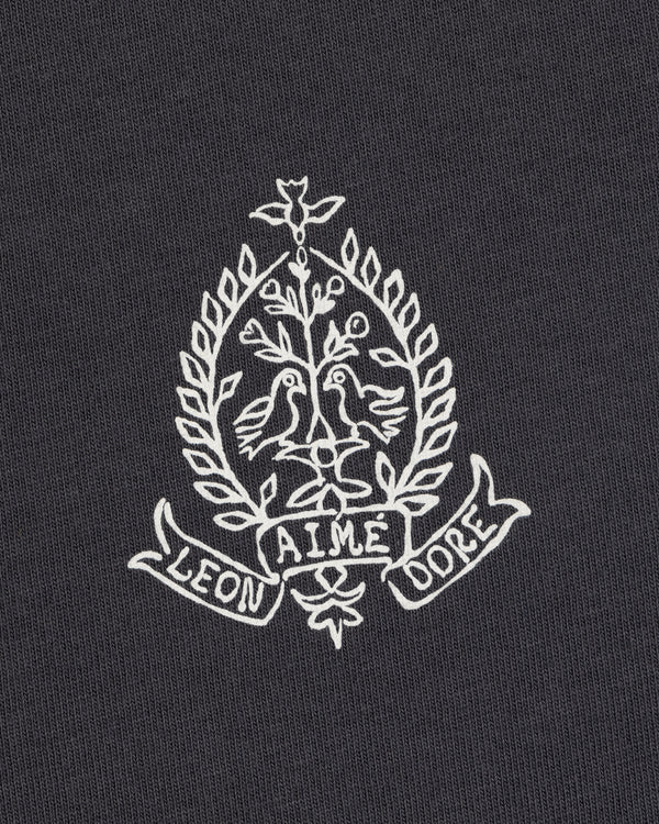 White crest with two birds, leaves, and "LEON AIME DOPE" on dark Saint George Graphic Tee.