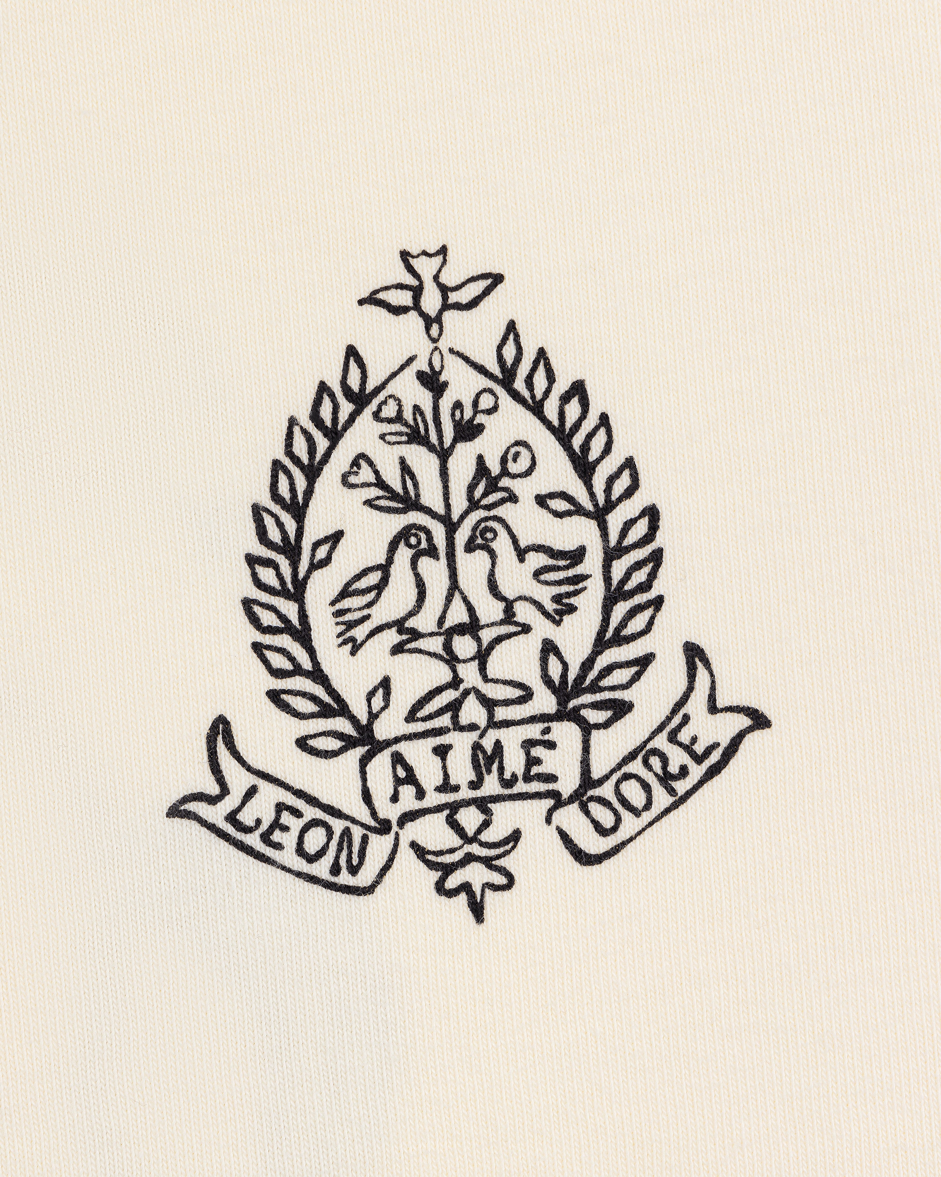 Cream Saint George Graphic Tee with embroidered crest featuring two birds, a tree, laurels, and “Aime Leon Dore” banner.