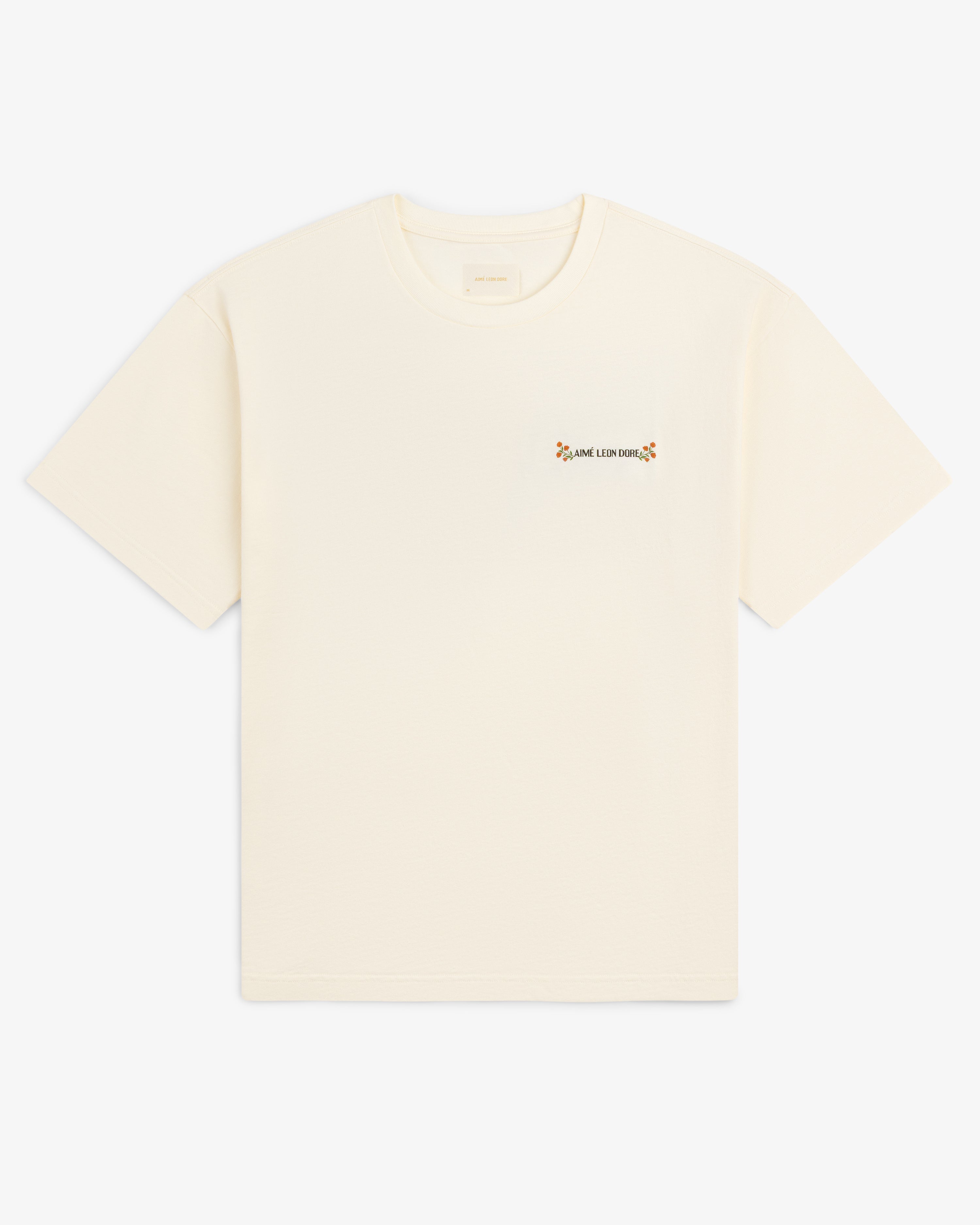 Aimé Postcard Tee: cream short-sleeve shirt with small text and a flower on the left chest.