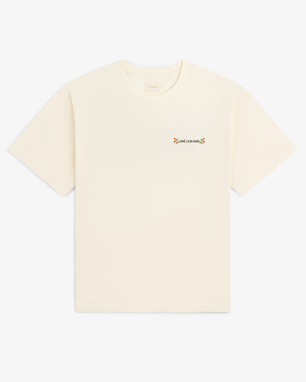 Aimé Postcard Tee: cream short-sleeve shirt with small text and a flower on the left chest.