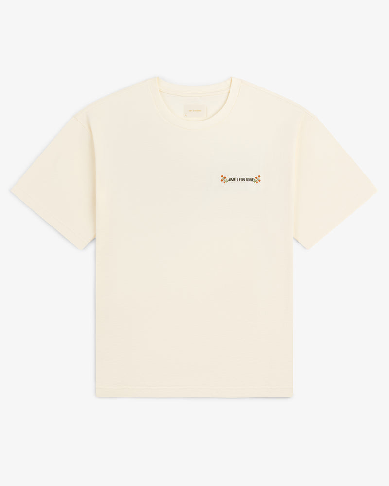 Aimé Postcard Tee: cream short-sleeve shirt with small text and a flower on the left chest.