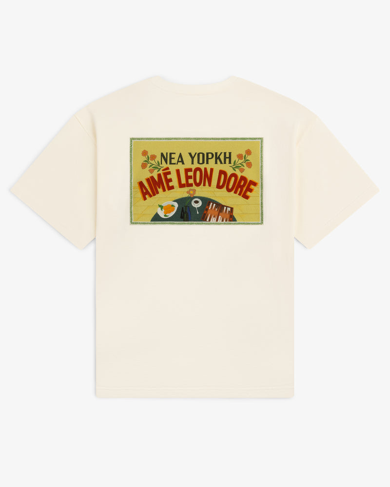 Cream Aimé Postcard Tee featuring a colorful postcard graphic and "Nea Yopkh Aime Leon Dore" on the back.
