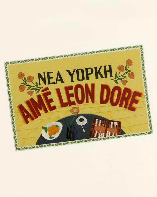 A yellow sign with flowers and a table is featured on the Aimé Postcard Tee by Aimé Leon Dore.