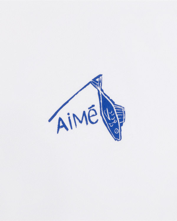 A blue fish illustration hangs on a line above the word AiMĒ on the white Fisherman Tee.