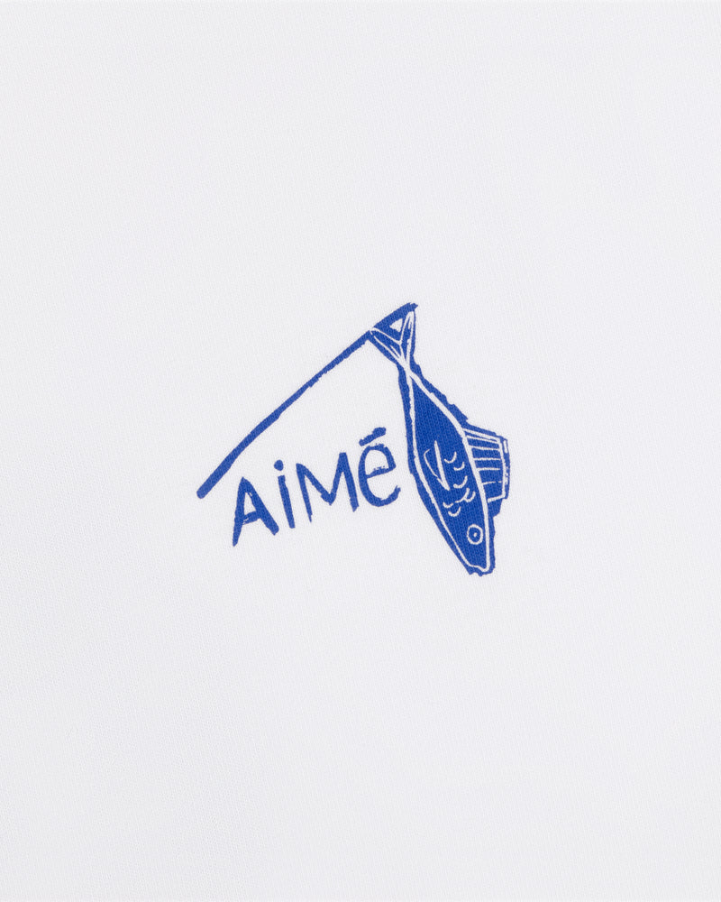 A blue fish illustration hangs on a line above the word AiMĒ on the white Fisherman Tee.