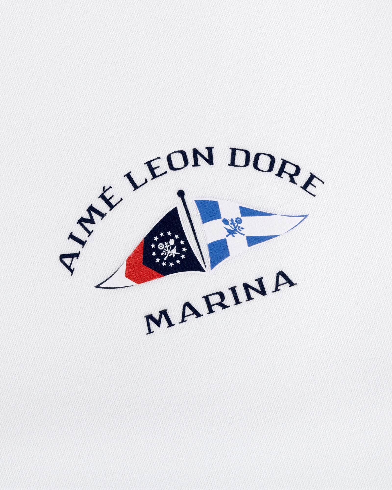 Marina Tee with embroidered Aimé Leon Dore Marina logo and two nautical flags on white fabric.