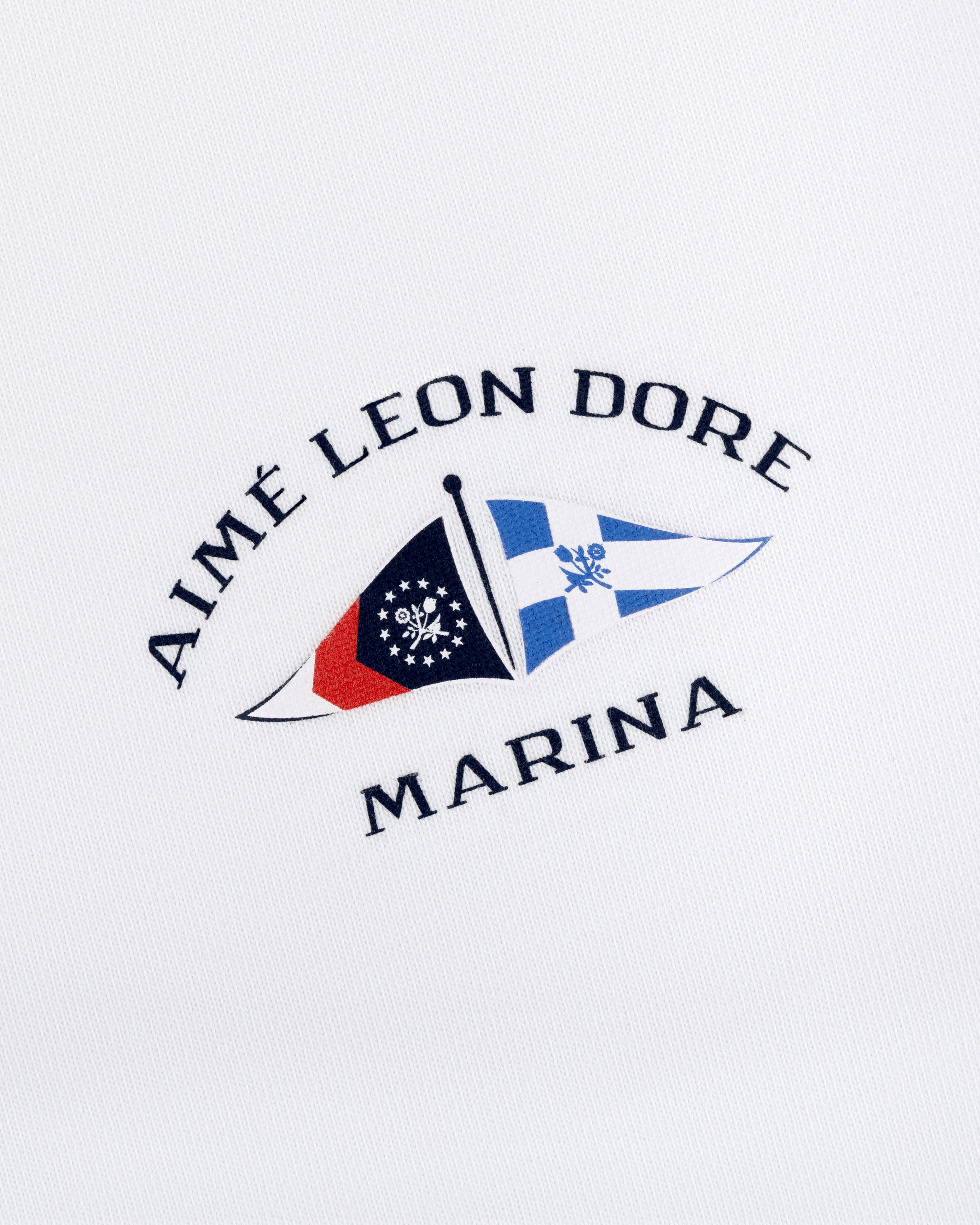 Marina Tee with embroidered Aimé Leon Dore Marina logo and two nautical flags on white fabric.