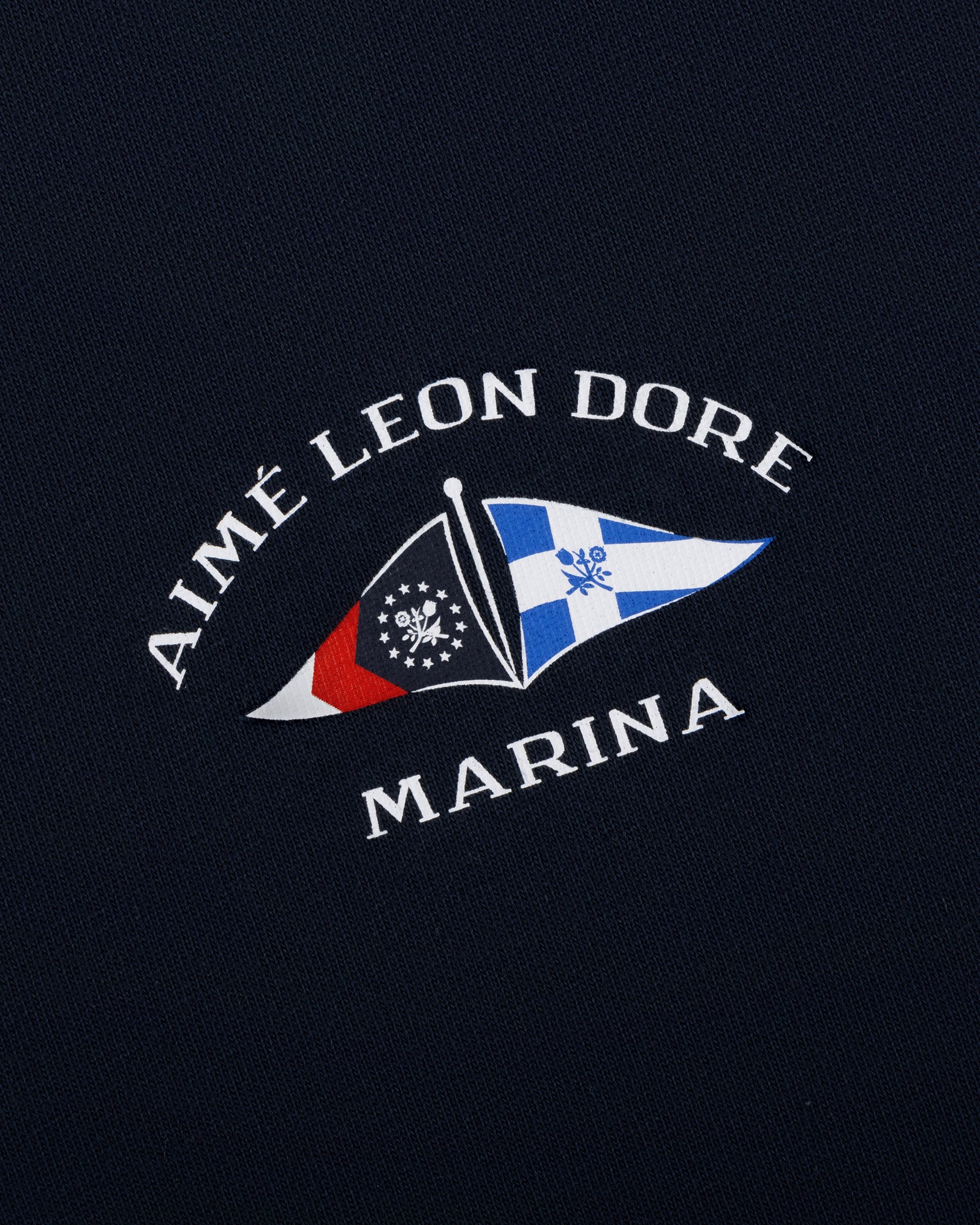 Navy Marina Tee with AIMÉ LEON DORE MARINA and two nautical flags in white, red, blue, and black.