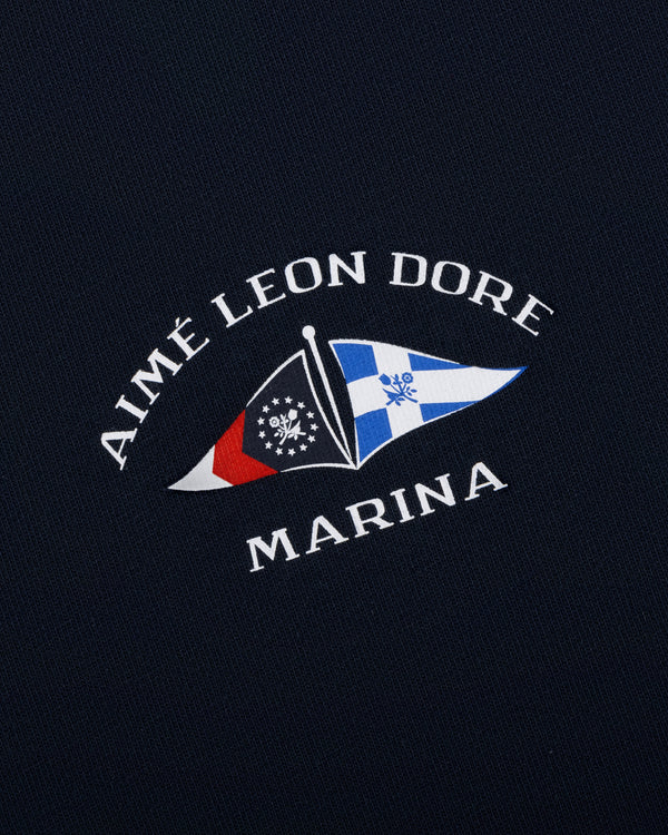 Navy Marina Tee with AIMÉ LEON DORE MARINA and two nautical flags in white, red, blue, and black.