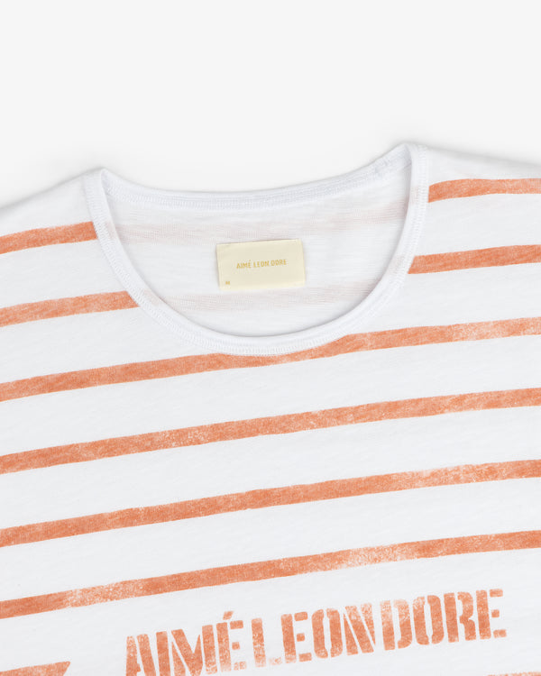 Slub Beach Tee: White T-shirt with orange stripes and AIMÉ LEON DORE text on the chest.