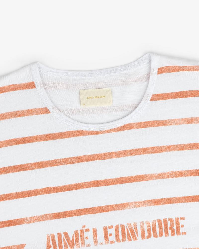 Slub Beach Tee: White T-shirt with orange stripes and AIMÉ LEON DORE text on the chest.