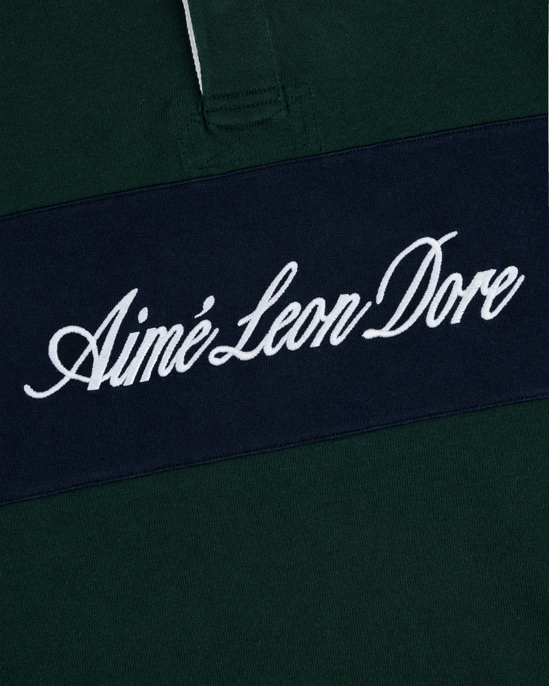 A close-up of the Script Paneled Rugby, a dark green shirt with Aimé Leon Dore in white on a navy stripe.