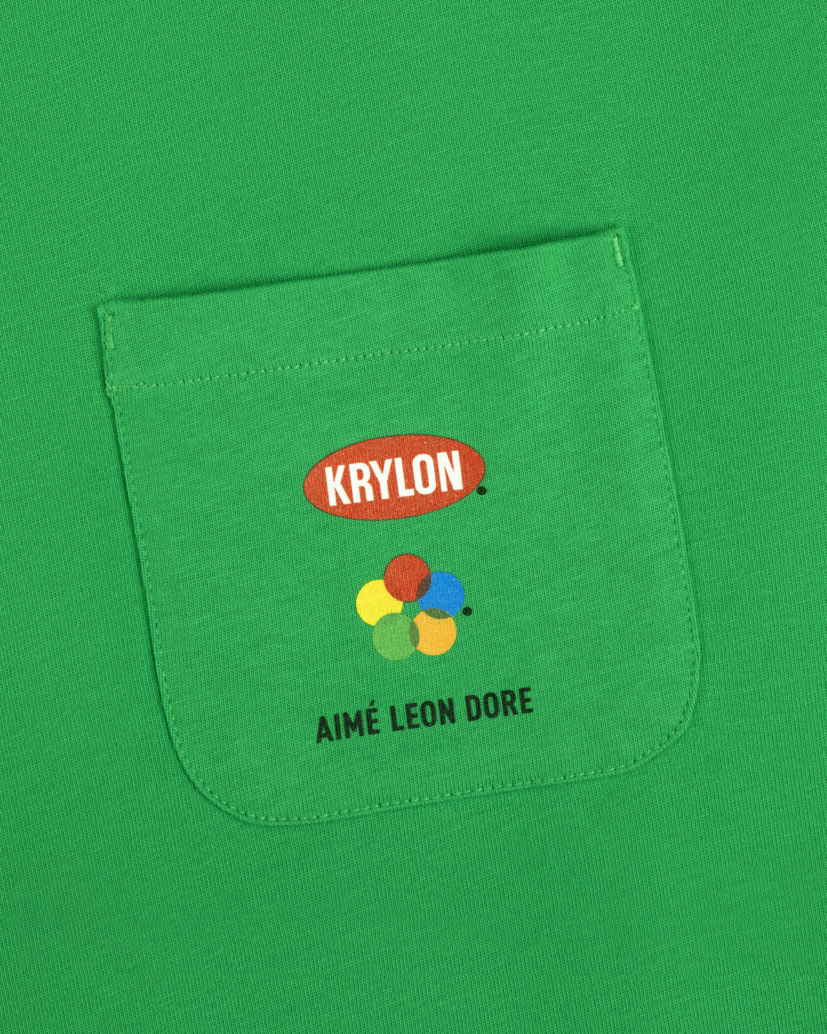 Krylon Pocket Tee with colorful paint dots and AIMÉ LEON DORE printed on the green shirt pocket.