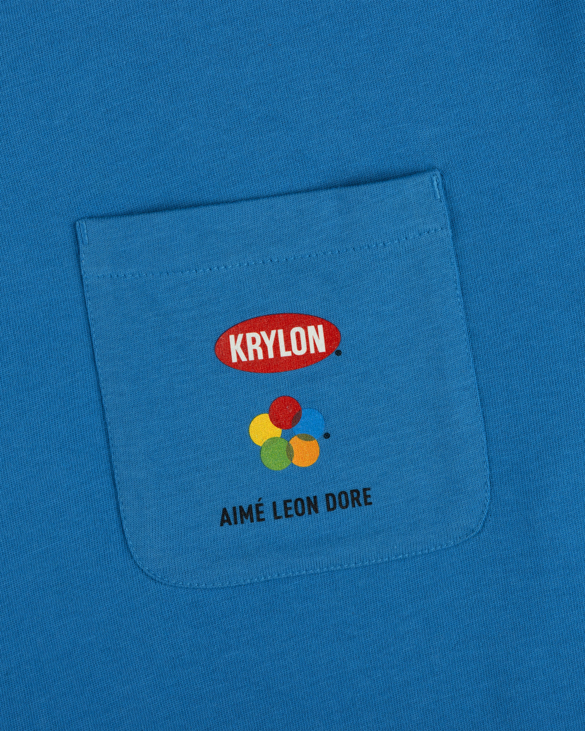 Krylon Pocket Tee: blue shirt with KRYLON logo, colorful paint blobs, and AIMÉ LEON DORE below the pocket.