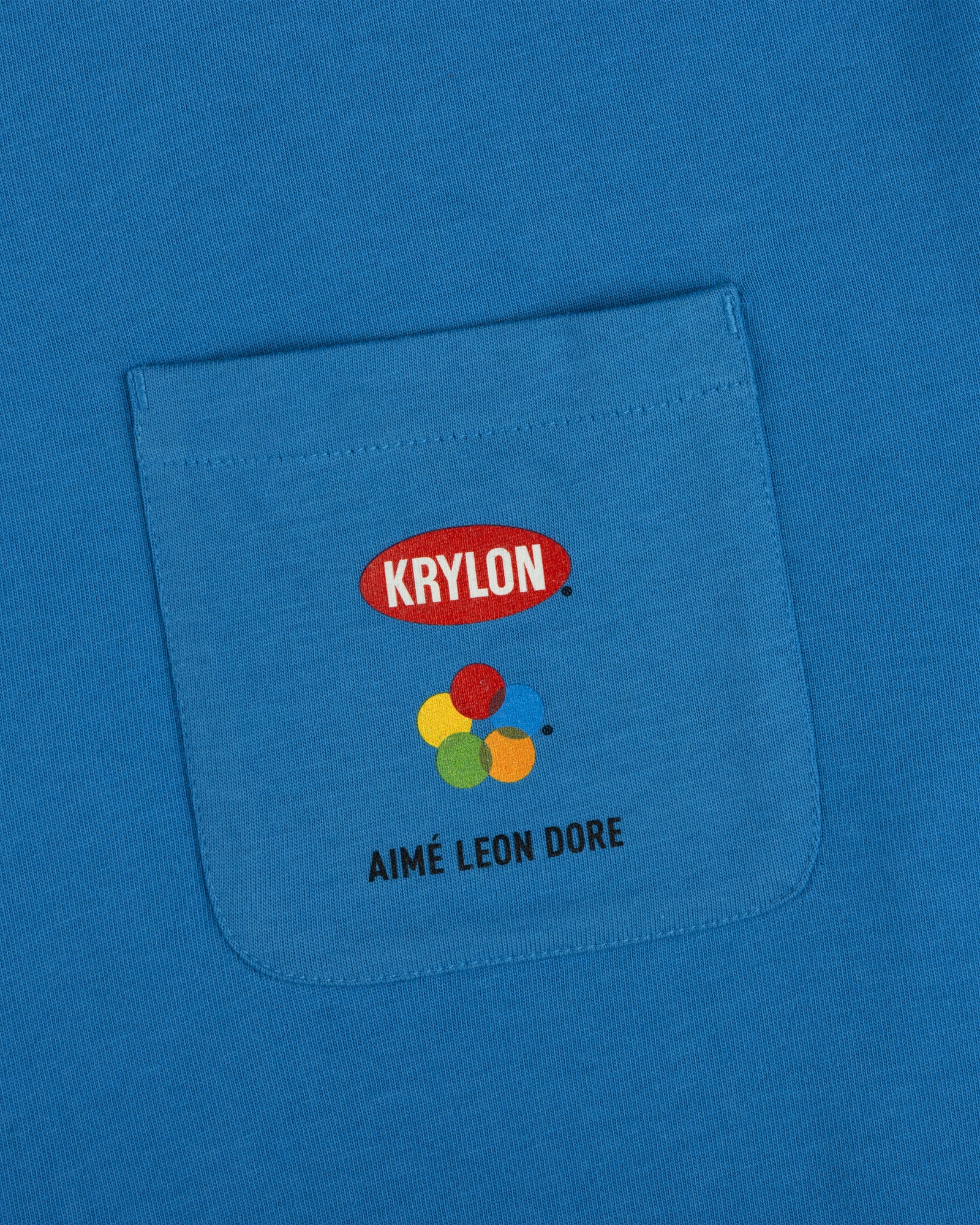Krylon Pocket Tee: blue shirt with KRYLON logo, colorful paint blobs, and AIMÉ LEON DORE below the pocket.
